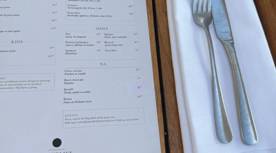 Houten tafel met menukaart en servies bij Republiek Bloemendaal, klaar voor lunch aan zee