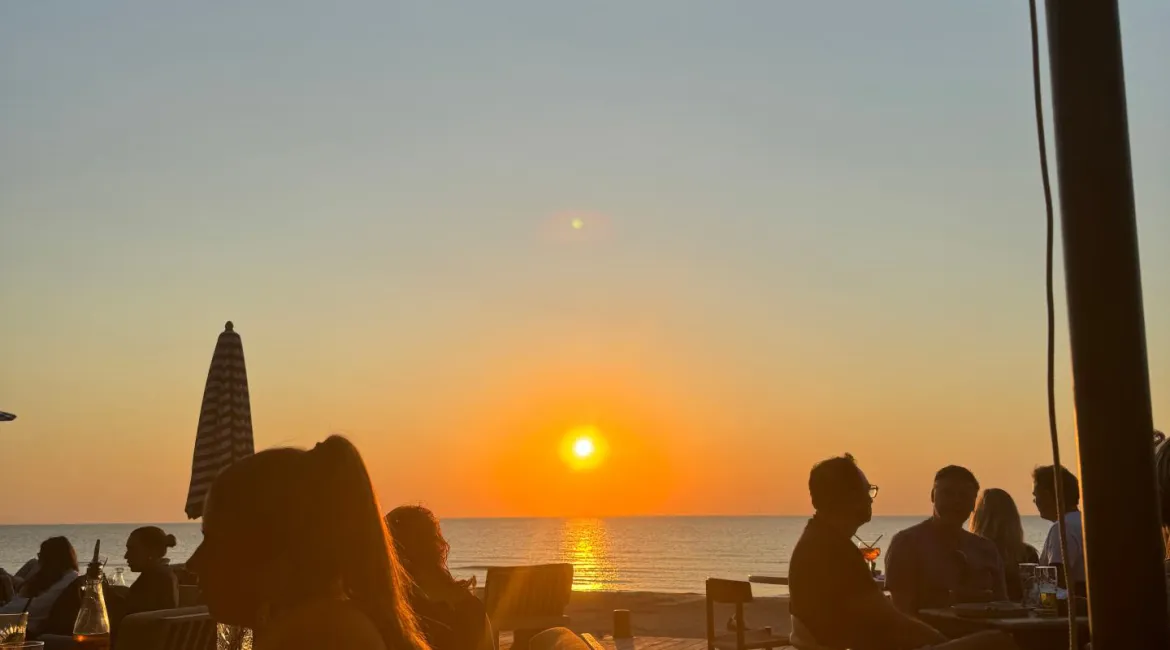 Zonsondergang bij Republiek Bloemendaal met gasten op het terras en uitzicht over zee
